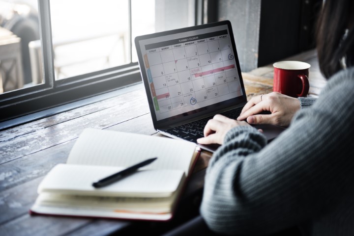 Partial shot of a male student using a laptop at a desktop with a book and a cup of coffee