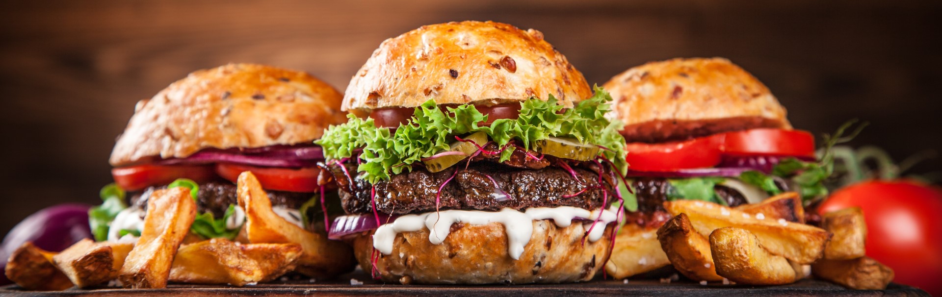 Three hamburgers layed out with french fries on a table