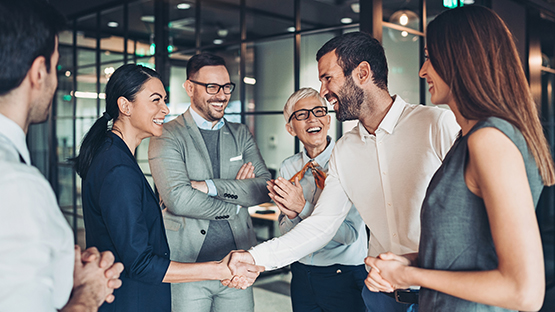 A group of people smiling and cherring while two of them are shaking hands.
